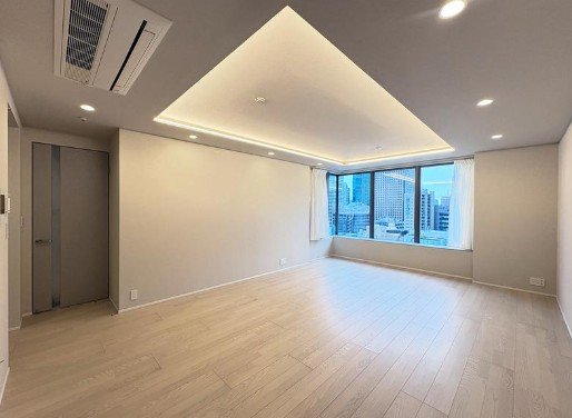 空の部屋、木製の床、天井には間接照明、窓から都市の景色が見える