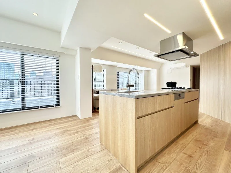 明るいリビングとキッチンのオープンな空間。木製のカウンターと窓からの自然光が特徴です。