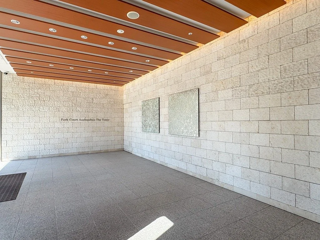 石の壁と木製の天井を持つ建物のロビー。左側に入り口のマットが見える。壁に「Park Court Azabu-juban The Tower」と書かれている。
