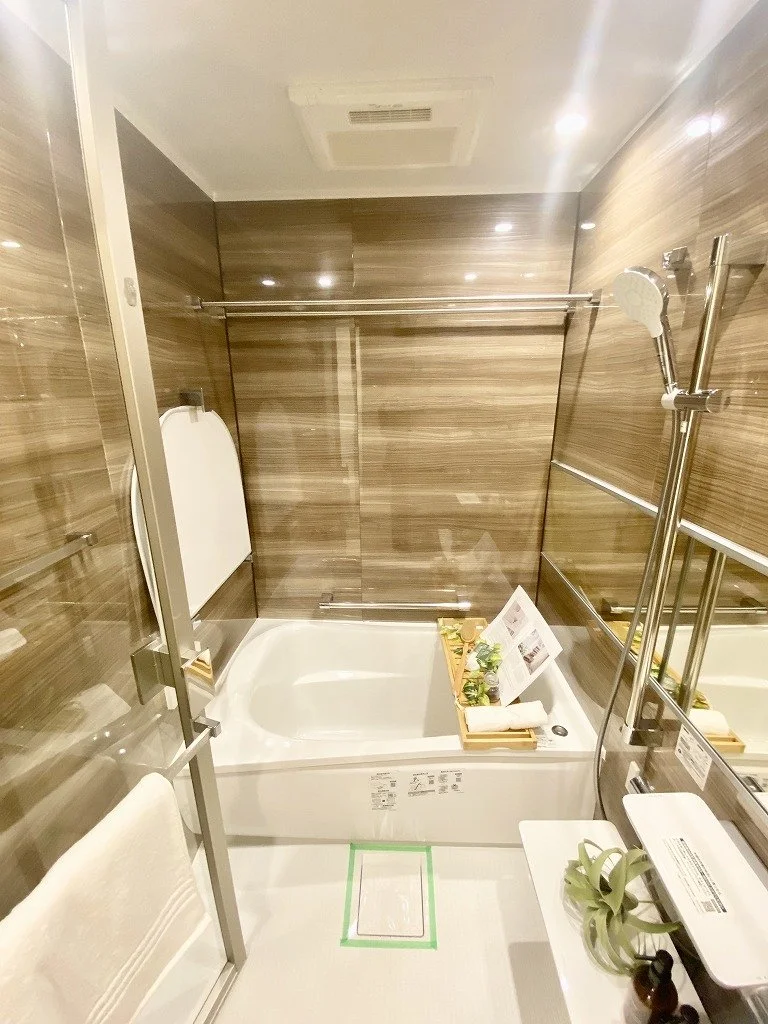 バスルームの浴槽とシャワー、鏡、タオルホルダー、グリーンの植物と小物が置かれた洗面台のある現代的なバスルーム