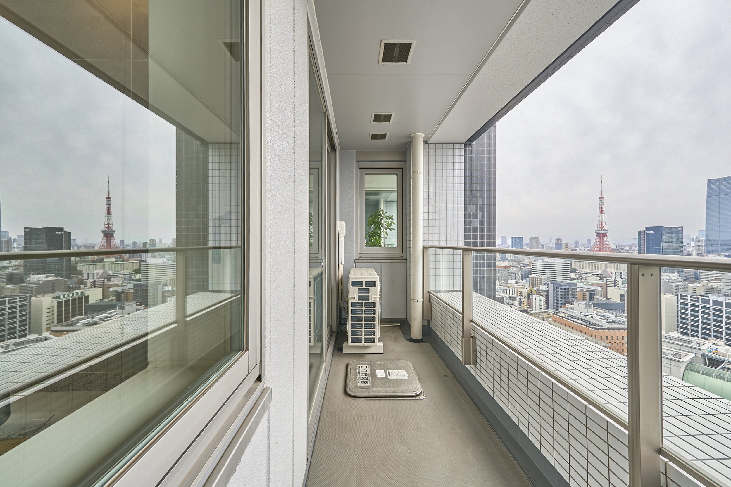 高層ビルの屋上のバルコニーから東京の都市景観を眺める。東京タワーやビル群が見える。