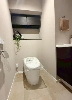 トイレと洗面所の小さな部屋の内観。トイレと洗面台があり、壁に小さな棚とタオル掛けが設置されている。