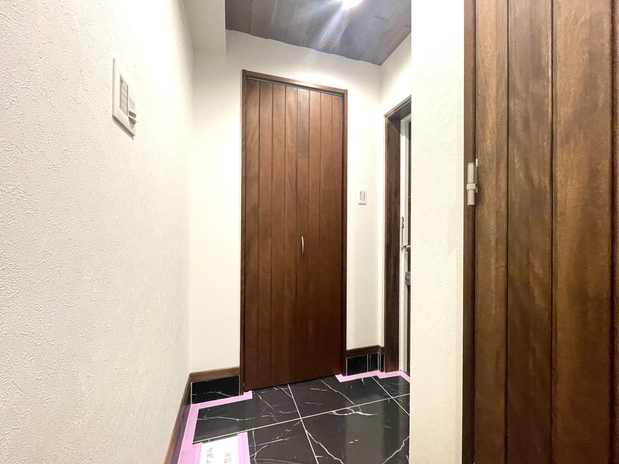 木製のドア。壁は白色で、黒と白のタイルの床。