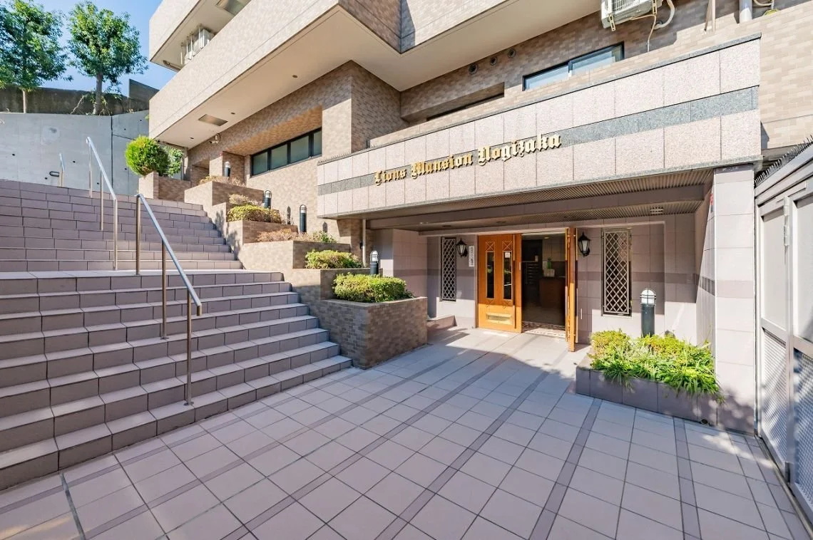 高層マンションの入り口と階段、植物と照明が配置されたエントランス