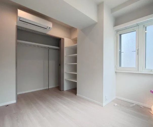 白い壁の部屋で、窓、エアコン、空のクローゼットと棚がある部屋