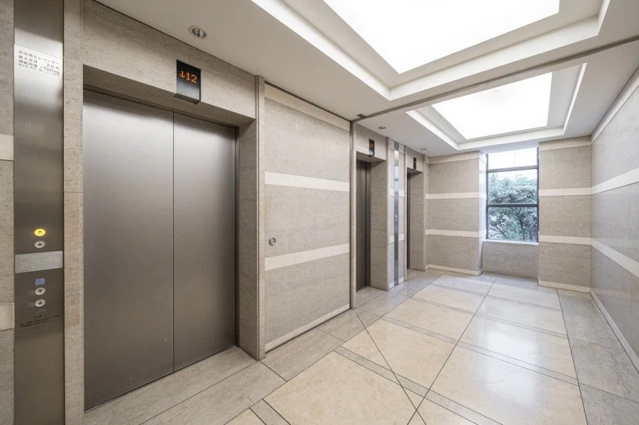 エレベーターの入り口、階数表示は「12階」、明るい自然光の差し込むエレベーターホールの内装