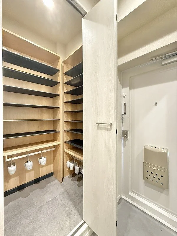 靴や傘を収納するための棚とパイプが設置されたシューズクロークです。隣には玄関ドアが見えます。