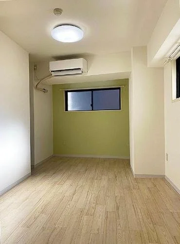 空の部屋、木製フローリング、白と緑の壁、天井の照明、エアコンと窓