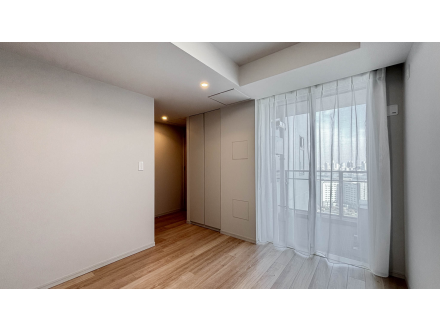 白い壁と木製の床、窓に白いカーテンが掛かっている空間。