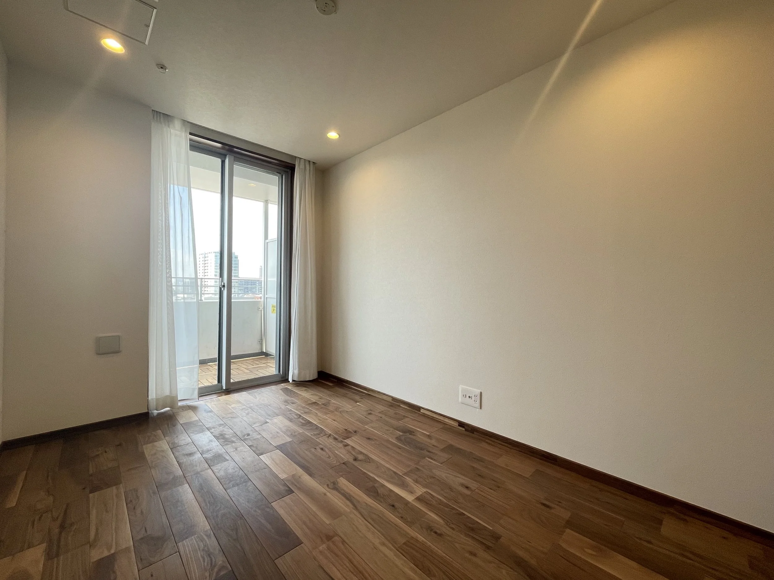 日当たりの良い空室の部屋、木製フローリングとバルコニーへのガラスドア。