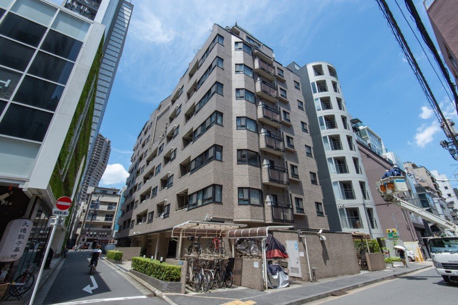 都市の高層マンションと自転車置き場、横断歩道のある交差点、青空と雲が見える街の風景