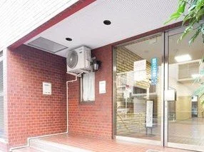 建物の入口のガラスドアと赤レンガの壁、空調機と電気メーターが見える