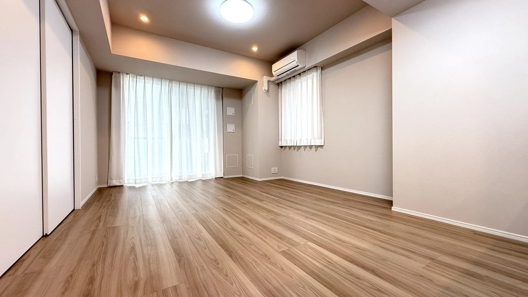 空の部屋、木製の床と白い壁、窓に白いカーテン、エアコン、天井にライト