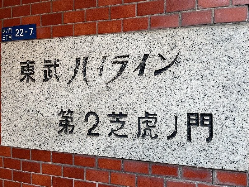 赤レンガの壁に設置された石の看板に、日本語とローマ字で書かれた住所と地名。