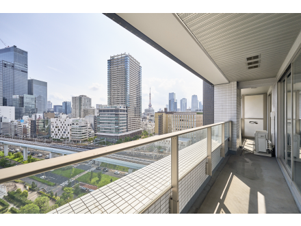 高層ビルのある都市の眺めを望むバルコニー。白いタイルの床と金属製の手すりが特徴。