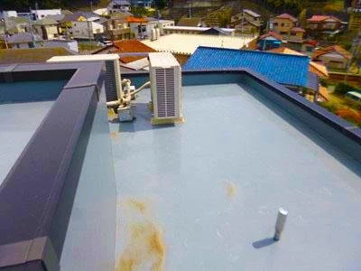 屋上の防水層。空気調和設備の配管と排気口が見える。周囲には住宅街が広がる。