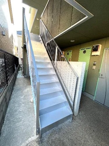 鉄製の階段と手すりがあるエレベーター付きの建物の外観。階段は白色で、上階へのアクセスを提供している。