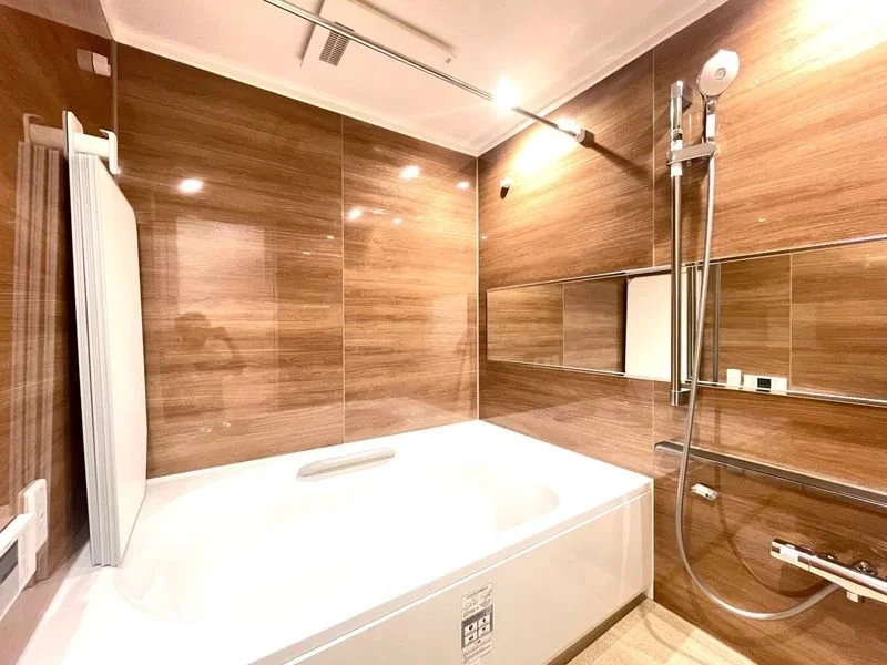 木目調の浴室で、白いバスタブとシャワーヘッドがあります。