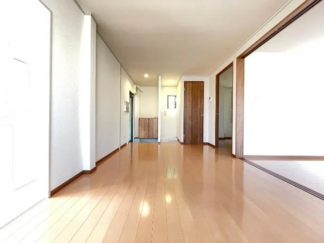 空のリビングルームの写真。木製のフローリングと白い壁、部分的にガラス引き戸とドアがあります。