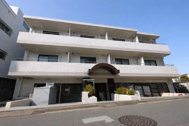 白い三階建ての建物で、正面にアーチ型の入口と低い生垣がある
