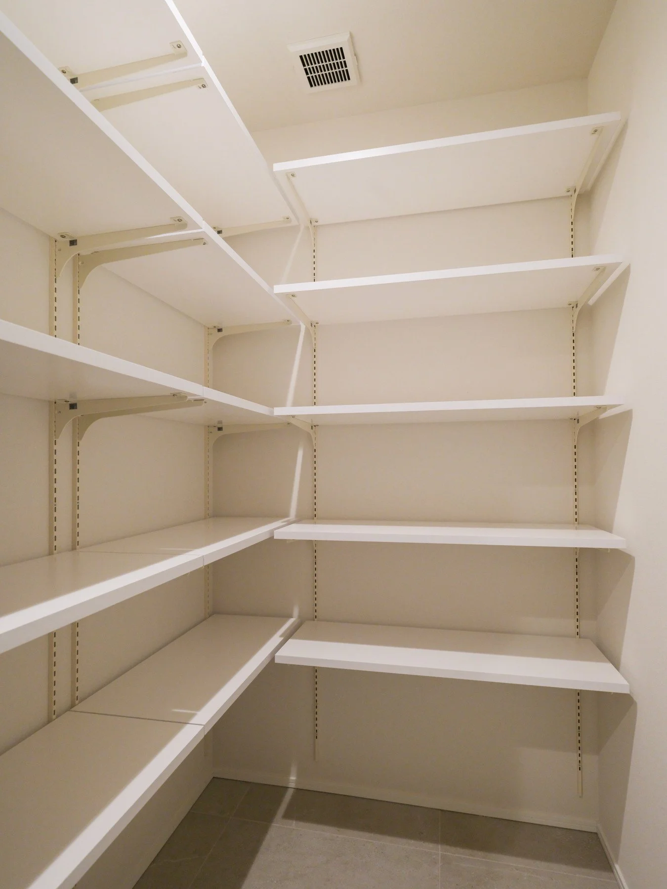 空の棚が設置された小さなクローゼットの内部。白い棚と壁、天井に換気扇や通気口があります。