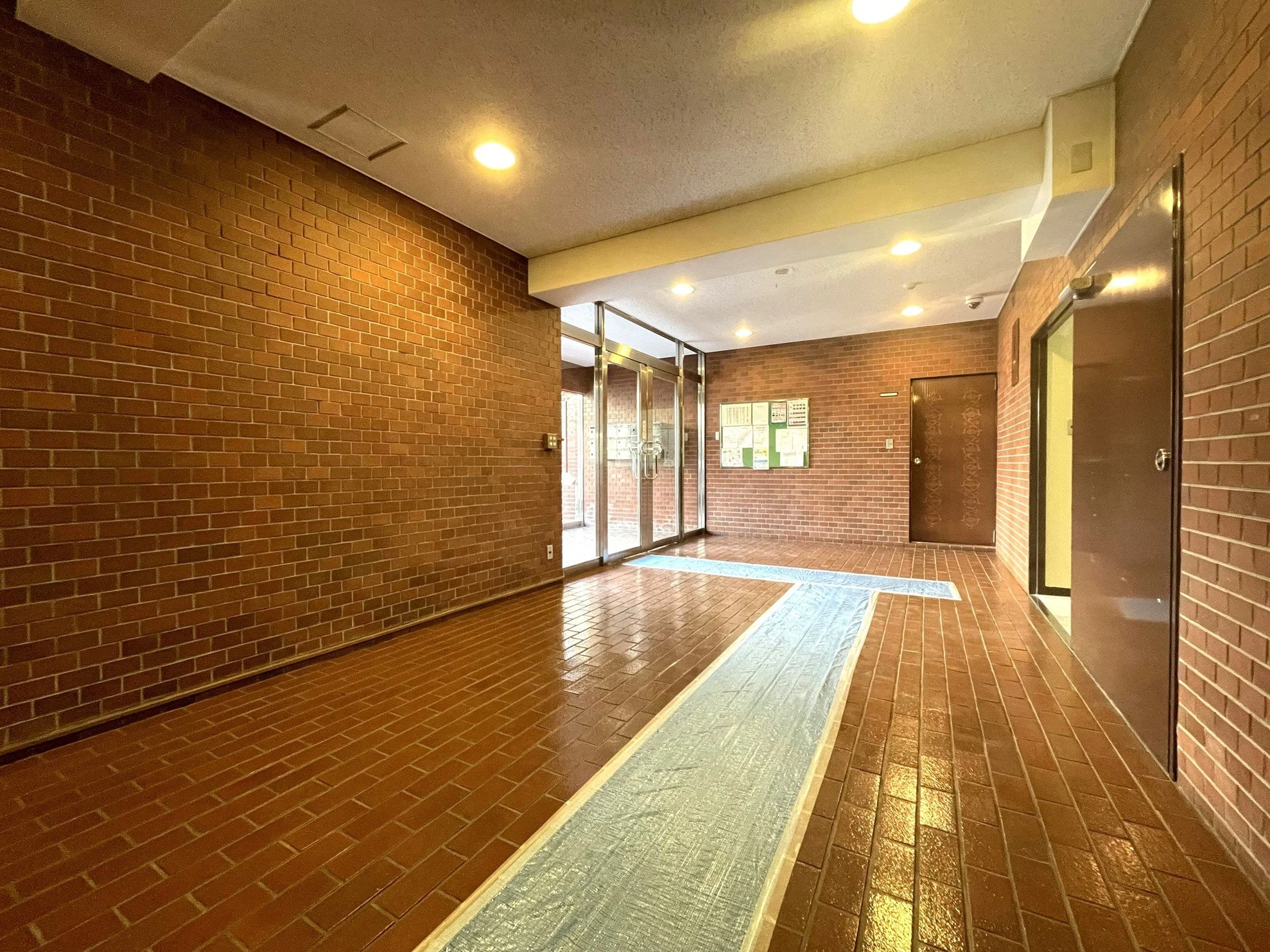 レンガ造りの建物のエントランスエリア、照明と掲示板が見える。
