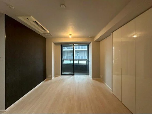 空の部屋で、バルコニーのある大きな窓、白い床、白い棚と黒い壁が特徴的です。