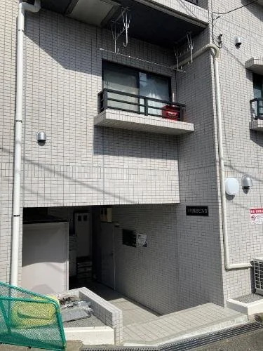 コンクリートのマンションのエントランスとバルコニー。バルコニーには洗濯物の干し竿と荷物が置かれている。
