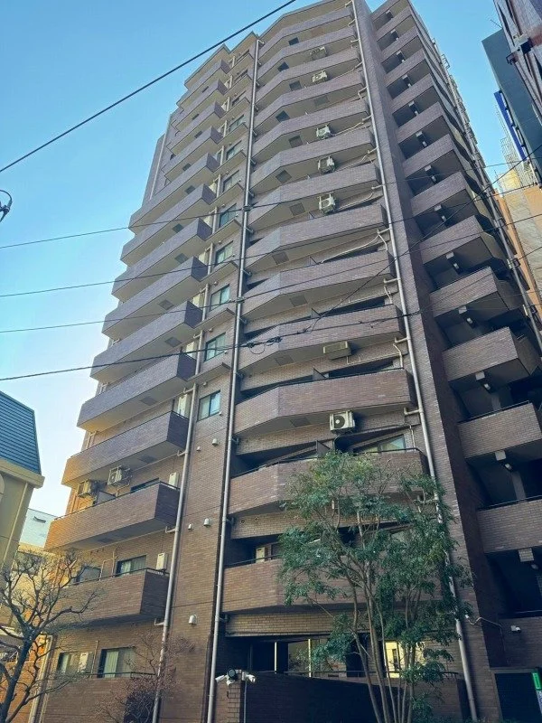 高層の集合住宅の外観。青空の下に建つ、ブロック状のバルコニーとエアコンのある窓が見えるマンションです。