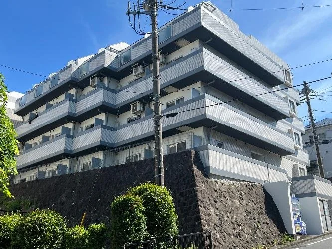 四階建ての白と灰色のアパートメントビル、青空の下にあります。