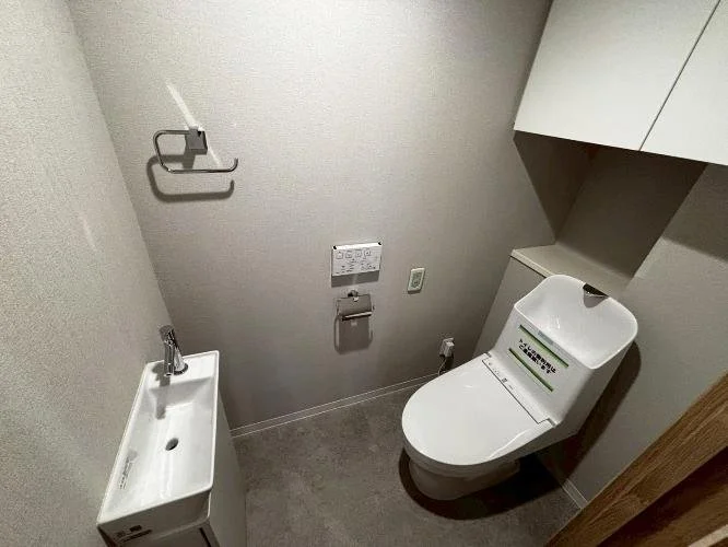 トイレと小さな洗面台、タオル掛けとリモコン付きの便座のあるこじんまりとしたトイレルーム