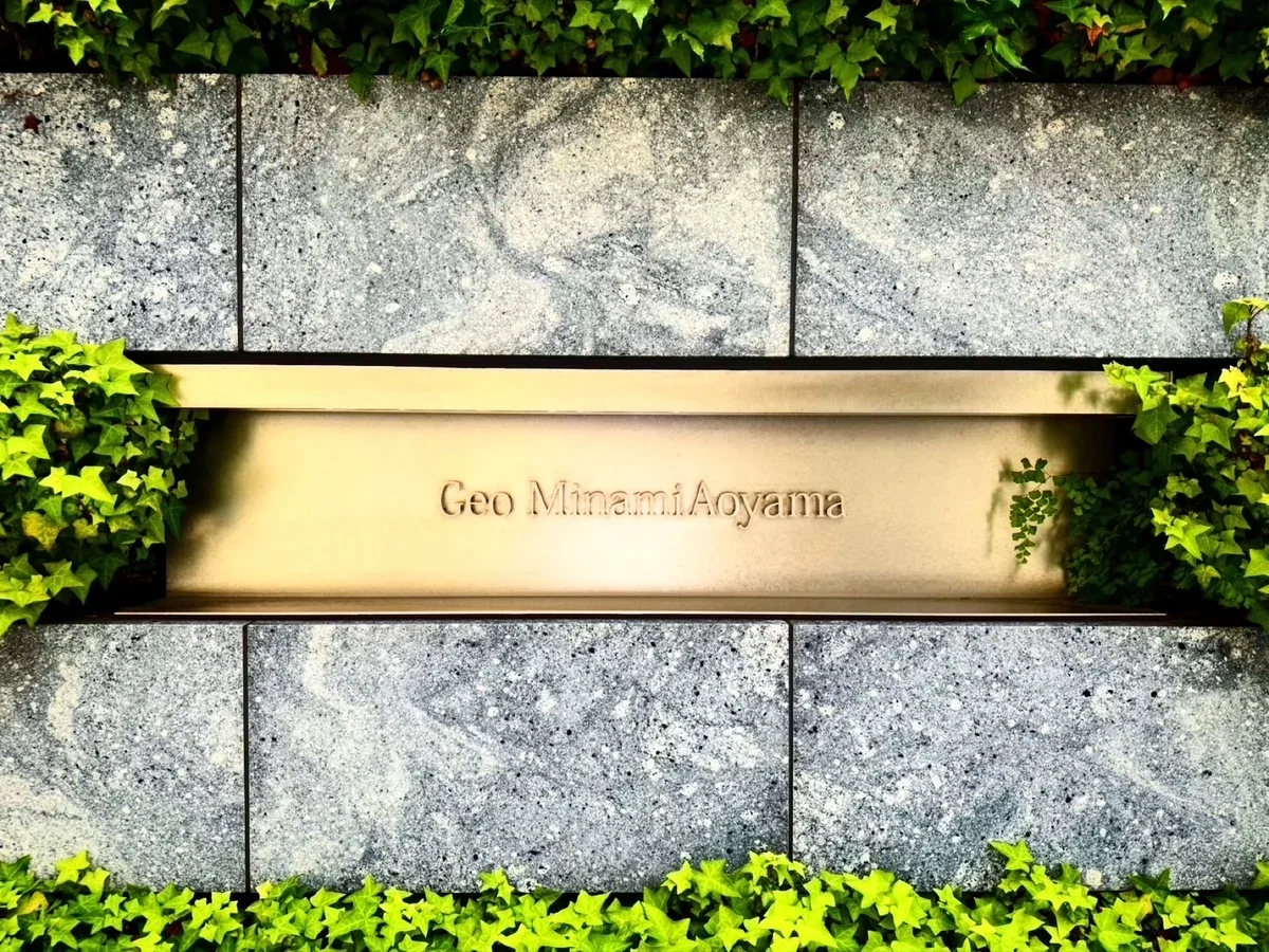 石の壁の上部に緑の葉があり、その下に金色のプレートに「Geo MinamiAoyama」と刻まれている。