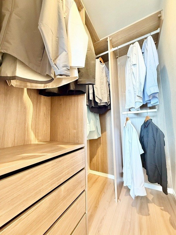 木の棚やハンガーにかかったシャツやコートが収納されたクローゼットの内部画像