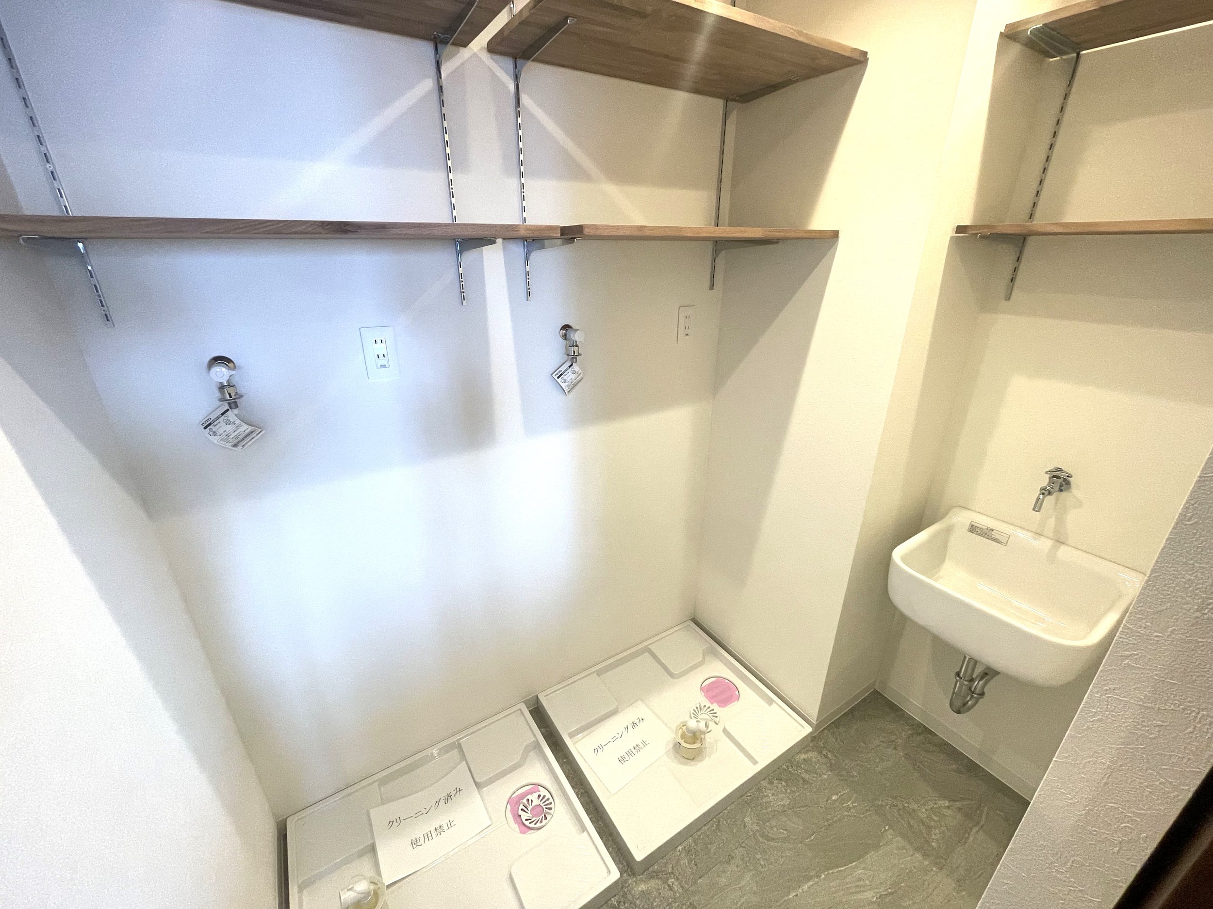 空の洗濯機置き場と洗濯用シンク、小さな棚が付いた壁面のクローゼットスペース