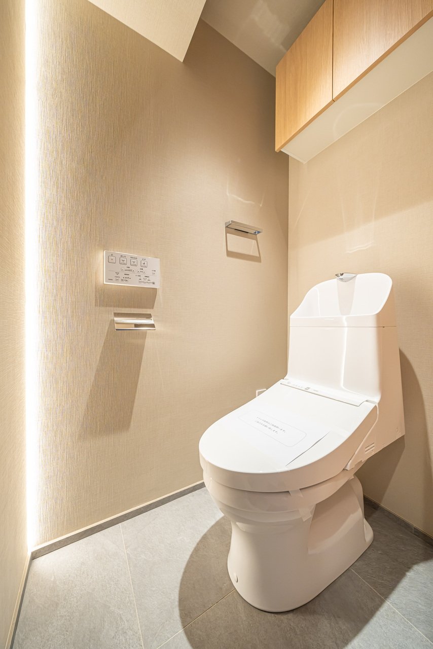 清潔で現代的なトイレです。壁に紙巻きトイレットペーパーと操作パネルがあり、木製の棚と壁ライトが付いています。