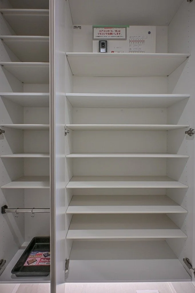 空の白い靴棚とハンガーラック。奥に電子レンジと小型の機器が置かれた棚がある。