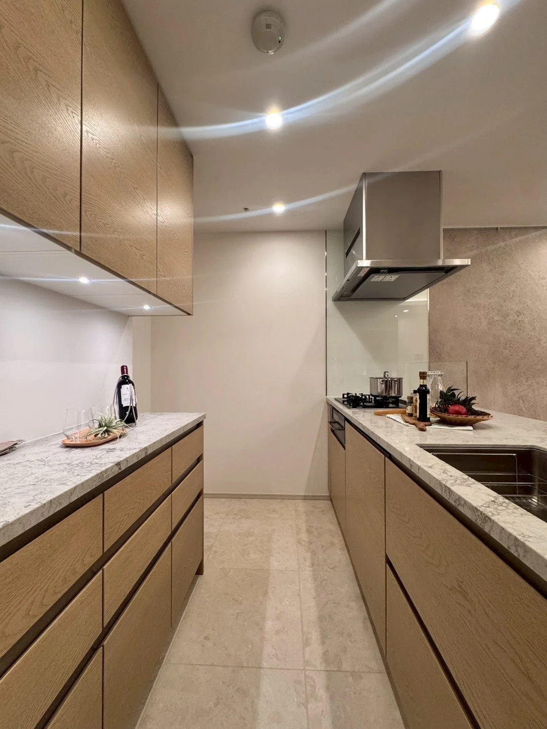 モダンな台所の interior, 木製のキャビネットと白い大理石のカウンター, ガスコンロとシンク, 食料品と調味料のボトル, ワインとグラス