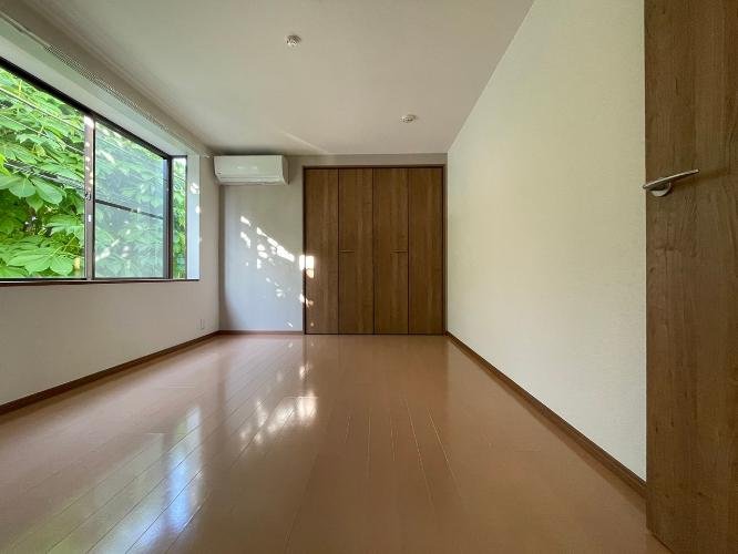 空の部屋、木製の床と壁の引き戸、窓から緑の木々が見える。