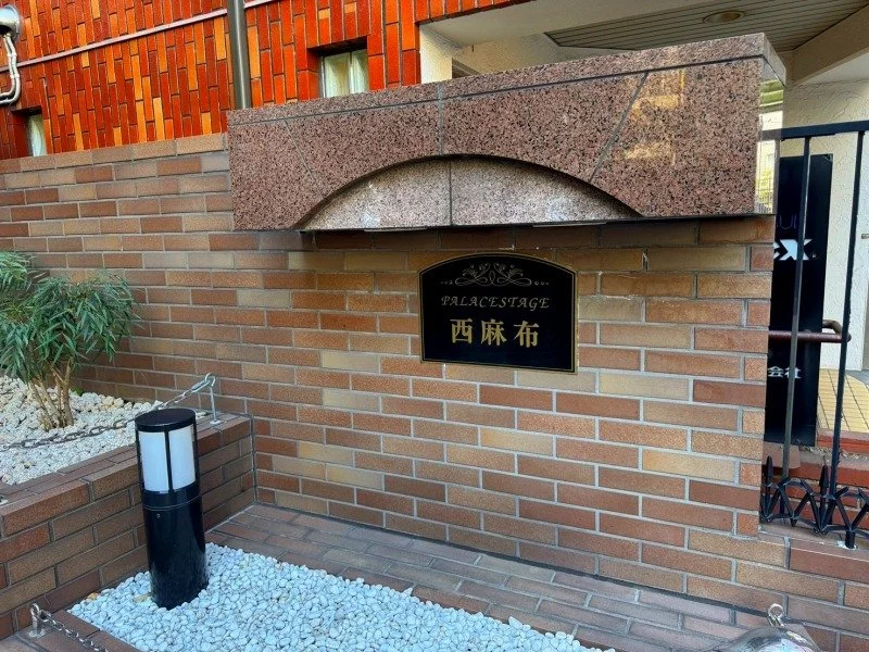 レンガの壁や石の表札に書かれた看板と、植えられた植物や照明が見える入口の風景.