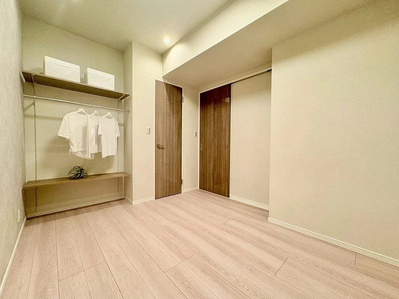 空の部屋、壁にハンガーラックと衣服、木製の扉がある