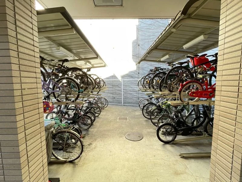 二階建ての自転車置き場に多くの自転車が駐車されている写真。屋根付きで、周囲に囲いがある。」}