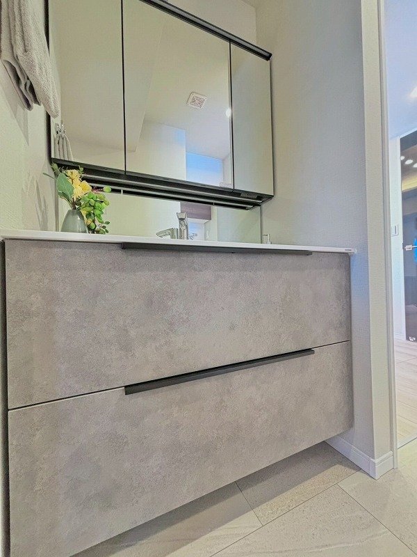 鏡張りの扉の洗面台と洗面鏡、上に花の飾りが置かれている洗面所の内装