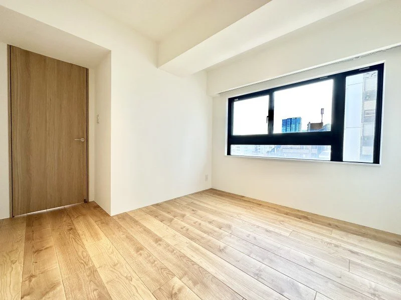 白い壁と木製の床、黒い縁の大きな窓がある空き部屋