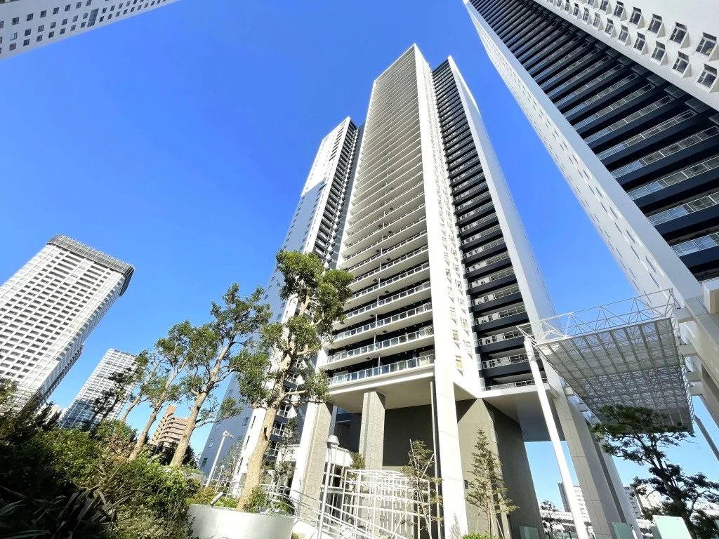 高層ビル群と青空。低層の植木と歩道が見える都市の風景。