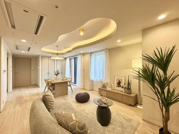 明るく広々としたリビングルームのインテリア。ソファ、円形のラグ、テレビ台、観葉植物、ダイニングテーブルと椅子が見える。