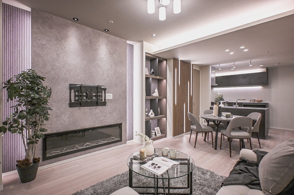 モダンなリビングルームの画像で、ソファ、コーヒーテーブル、ダイニングテーブルと椅子、キッチン、飾り棚、植物、暖炉が見える。