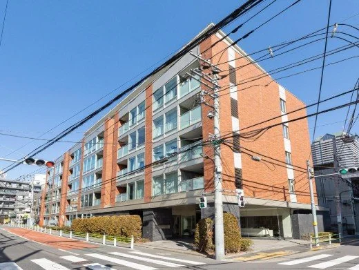 多階建てのコンクリート建築のマンションと電線、バス停と歩道がある都市風景