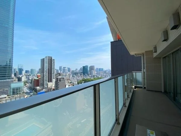 高層ビルのバルコニーから見た都市の景色。青空と多くのビルが見える。」}]}