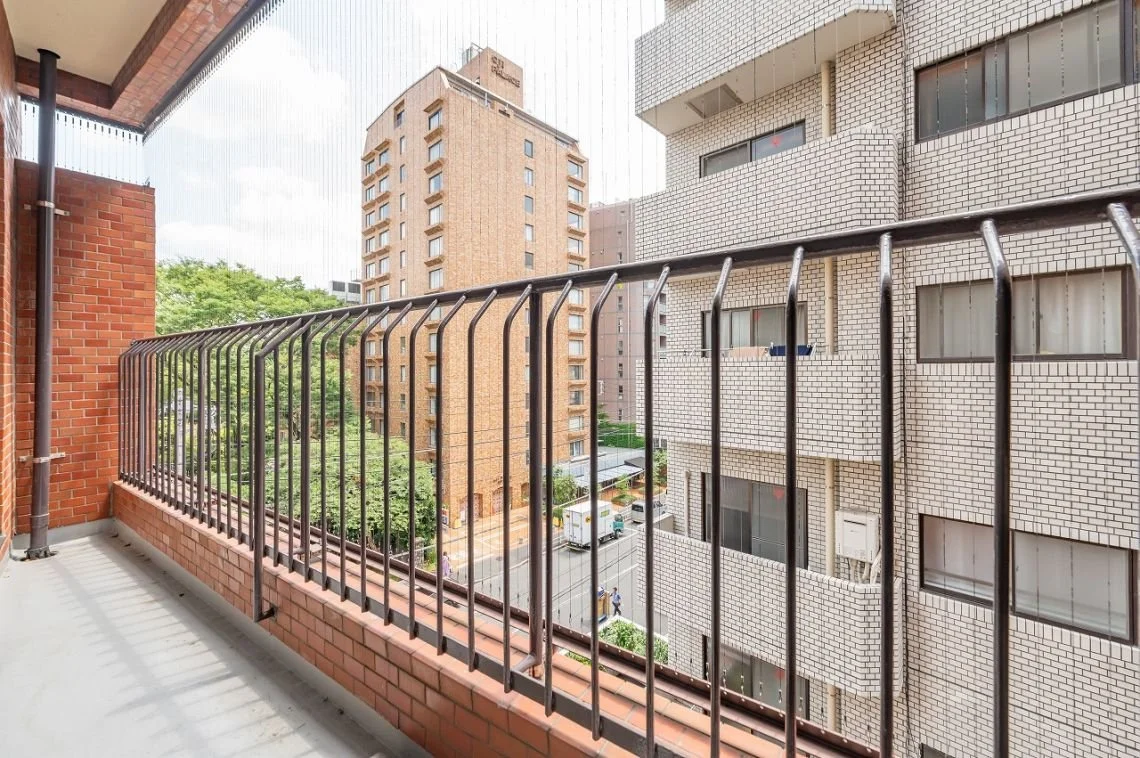 中層のマンションのバルコニーから見た景色。隣接した高層ビルと道路、車や人々が通る様子が写っている。