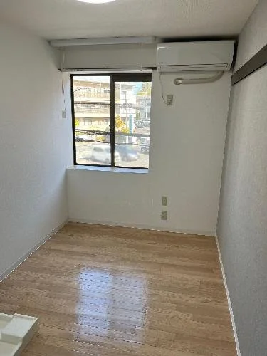 空の部屋、木製の床に窓とエアコン、白い壁とカーテンレールがあるです。